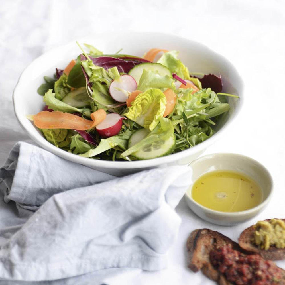 White kitchen scene with a fresh salad and a small cup of oil and vinegar for dressing showcasing light and vibrant white balsamic options.