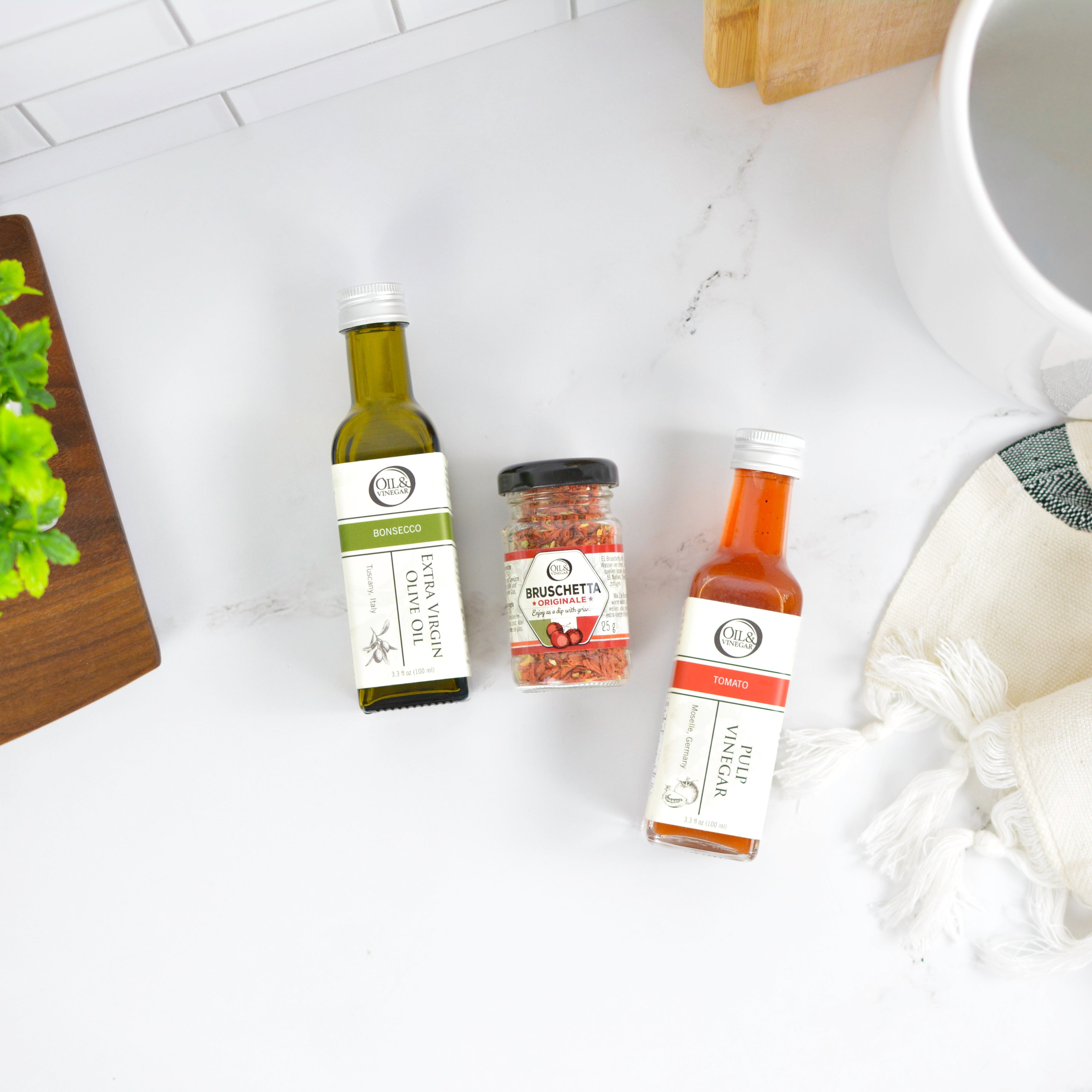 Collection of olive oil and balsamic vinegar bottles on a white surface with a wooden cutting board.